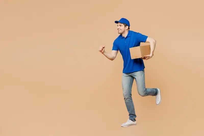 Paketbote in blauem Poloshirt läuft mit einem Paket unter dem Arm